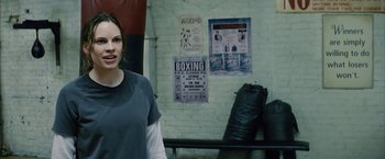 Movie still from “Million Dollar Baby” (2004), directed by Clint Eastwood – A woman standing in front of a wall with posters on it; Close Up shot, Over the shoulder angle