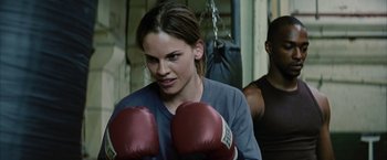 Movie still from “Million Dollar Baby” (2004), directed by Clint Eastwood – A woman wearing red boxing gloves in a boxing ring; Close Up shot, Over the shoulder angle