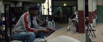 Movie still from “Million Dollar Baby” (2004), directed by Clint Eastwood – An older man sitting on the floor looking at a magazine; Medium shot, Low angle