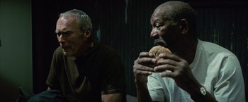 Movie still from “Million Dollar Baby” (2004), directed by Clint Eastwood – Two older men sitting next to each other eating a sandwich; Medium shot, Low angle