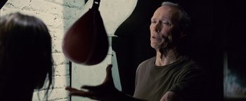 Movie still from “Million Dollar Baby” (2004), directed by Clint Eastwood – An older man holding a punching bag in front of a wall; Close Up shot, Low angle