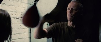 Movie still from “Million Dollar Baby” (2004), directed by Clint Eastwood – A bald man in a brown t - shirt throws a punching bag; Close Up shot, Low angle