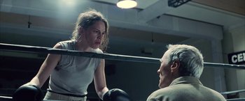 Movie still from “Million Dollar Baby” (2004), directed by Clint Eastwood – A woman in a boxing ring getting ready to punch a man in the head; Medium shot, Over the shoulder angle