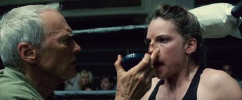 Movie still from “Million Dollar Baby” (2004), directed by Clint Eastwood – A woman in a boxing ring taking a sip from a cup; Close Up shot, Over the shoulder angle
