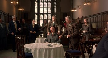 Movie still from “A Beautiful Mind” (2001), directed by Ron Howard – A group of men standing around a table with food; Wide shot, High angle