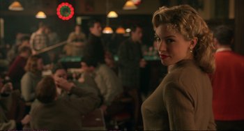 Movie still from “A Beautiful Mind” (2001), directed by Ron Howard – A woman standing in front of a group of people in a room; Medium shot, Over the shoulder angle