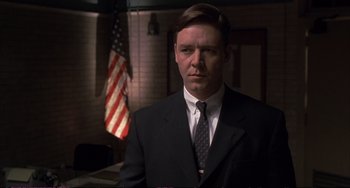 Movie still from “A Beautiful Mind” (2001), directed by Ron Howard – A man in a suit and tie in front of an american flag; Medium shot, Low angle