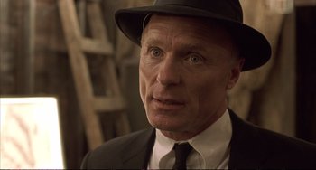 Movie still from “A Beautiful Mind” (2001), directed by Ron Howard – An older man wearing a suit and a hat; Close Up shot, Over the shoulder angle