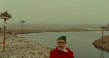 Movie still from “Moonrise Kingdom” (2012), directed by Wes Anderson – An older man wearing a green hat standing in front of a body of water; Medium shot, Over the shoulder angle
