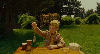 Movie still from “Moonrise Kingdom” (2012), directed by Wes Anderson – A young boy in a scout uniform holding a string of string; Medium shot, High angle