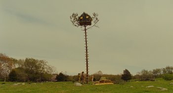 Movie still from “Moonrise Kingdom” (2012), directed by Wes Anderson – Two men standing next to a tree with a bird house on it; Extreme Wide shot, Low angle