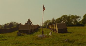 Movie still from “Moonrise Kingdom” (2012), directed by Wes Anderson – An american flag on top of a flag pole in a field; Extreme Wide shot, Low angle