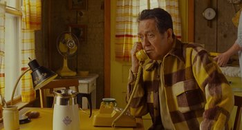 Movie still from “Moonrise Kingdom” (2012), directed by Wes Anderson – An older man sitting at a table talking on the phone; Medium shot, High angle