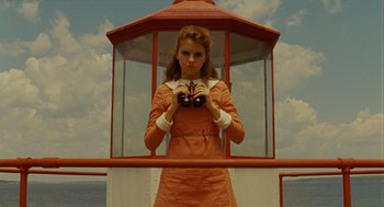 Movie still from “Moonrise Kingdom” (2012), directed by Wes Anderson – A woman standing in front of a lighthouse looking through binoculars; Medium shot, Low angle