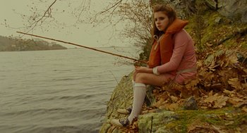 Movie still from “Moonrise Kingdom” (2012), directed by Wes Anderson – A woman sitting on a rock holding a fishing pole; Medium shot, High angle