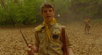 Movie still from “Moonrise Kingdom” (2012), directed by Wes Anderson – A young boy in scout uniform holding a bow and arrow; Medium shot, Over the shoulder angle