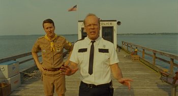 Movie still from “Moonrise Kingdom” (2012), directed by Wes Anderson – Two men standing on a dock near a body of water; Medium shot, Low angle