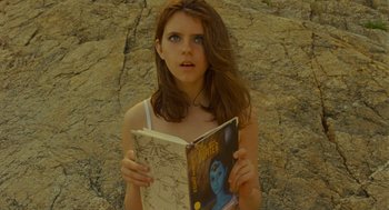 Movie still from “Moonrise Kingdom” (2012), directed by Wes Anderson – A woman holding an open book while standing in front of rocks; Close Up shot, Overhead angle