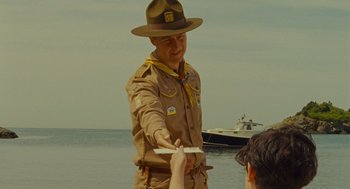 Movie still from “Moonrise Kingdom” (2012), directed by Wes Anderson – A man in a uniform is handing something to another man; Medium shot, Over the shoulder angle