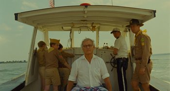 Movie still from “Moonrise Kingdom” (2012), directed by Wes Anderson – An older man sitting in front of a steering wheel on a boat; Medium shot, Low angle