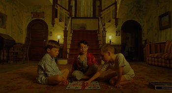 Movie still from “Moonrise Kingdom” (2012), directed by Wes Anderson – Three young boys sitting on the floor playing a board game; Wide shot, High angle