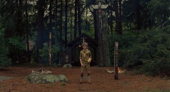 Movie still from “Moonrise Kingdom” (2012), directed by Wes Anderson – A boy scout standing in front of a wooden cross; Wide shot, Low angle