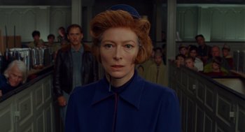 Movie still from “Moonrise Kingdom” (2012), directed by Wes Anderson – A woman in a blue coat standing in front of a group of people; Close Up shot, Low angle