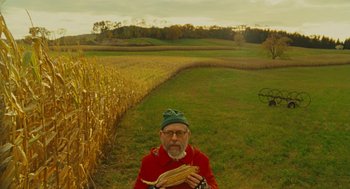 Movie still from “Moonrise Kingdom” (2012), directed by Wes Anderson – A man in a field holding a bundle of corn; Wide shot, High angle