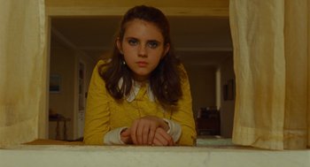 Movie still from “Moonrise Kingdom” (2012), directed by Wes Anderson – A girl in a yellow dress is sitting on a table; Medium shot, Low angle