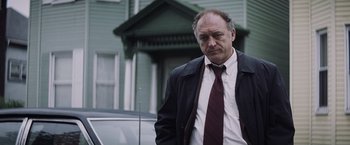 Movie still from “Mystic River” (2003), directed by Clint Eastwood – A man in a suit and tie standing in front of a building; Medium shot, Low angle