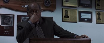 Movie still from “Mystic River” (2003), directed by Clint Eastwood – A man sitting at a desk in front of a plaque; Close Up shot, Low angle