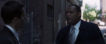 Movie still from “Mystic River” (2003), directed by Clint Eastwood – A man wearing a suit and tie standing in front of a brick building; Close Up shot, Over the shoulder angle