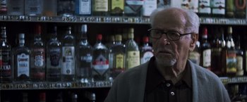 Movie still from “Mystic River” (2003), directed by Clint Eastwood – An older man with glasses in front of a shelf of alcohol; Close Up shot, Low angle