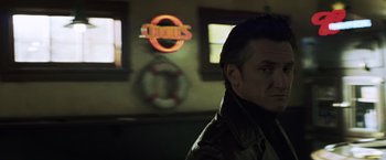 Movie still from “Mystic River” (2003), directed by Clint Eastwood – A man standing in front of a building with lights on; Close Up shot, Low angle