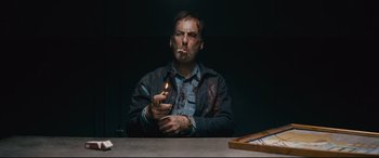 Movie still from “Nobody” (2021), directed by Ilya Naishuller – A man sitting at a table holding a lit candle; Medium shot, Overhead angle