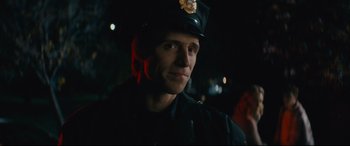 Movie still from “Nobody” (2021), directed by Ilya Naishuller – A man in a police officer's uniform is smiling for the camera; Close Up shot, Over the shoulder angle
