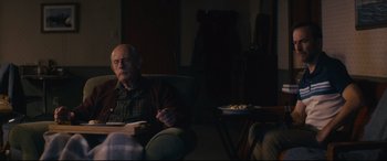 Movie still from “Nobody” (2021), directed by Ilya Naishuller – An older man sitting in a chair in a living room; Medium shot, Over the shoulder angle