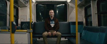 Movie still from “Nobody” (2021), directed by Ilya Naishuller – A man sitting on a bench on a train; Medium shot, Low angle