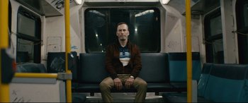 Movie still from “Nobody” (2021), directed by Ilya Naishuller – A man sitting on a bench on a train; Medium shot, Low angle