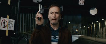 Movie still from “Nobody” (2021), directed by Ilya Naishuller – A man holding up a cell phone while standing in front of a car; Close Up shot, Low angle