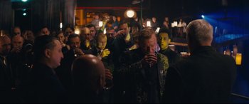 Movie still from “Nobody” (2021), directed by Ilya Naishuller – A group of people standing in a room with drinks; Medium shot, Over the shoulder angle