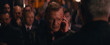Movie still from “Nobody” (2021), directed by Ilya Naishuller – A man is on a cell phone in front of a group of people; Close Up shot, Over the shoulder angle