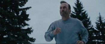 Movie still from “Nobody” (2021), directed by Ilya Naishuller – A man in a blue shirt is running outside; Close Up shot, Low angle