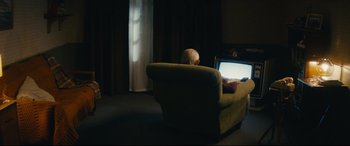 Movie still from “Nobody” (2021), directed by Ilya Naishuller – A person sitting on a couch looking at a computer screen; Wide shot, Low angle