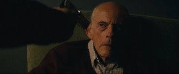 Movie still from “Nobody” (2021), directed by Ilya Naishuller – An old man sitting in a chair with a gun in his hand; Close Up shot, High angle