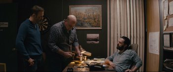 Movie still from “Nobody” (2021), directed by Ilya Naishuller – Two men sitting at a table in front of a painting; Medium shot, Over the shoulder angle
