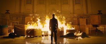 Movie still from “Nobody” (2021), directed by Ilya Naishuller – A man standing in front of a large fire; Wide shot, Low angle