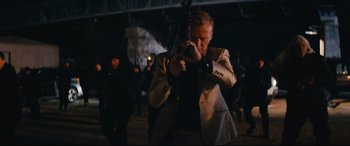 Movie still from “Nobody” (2021), directed by Ilya Naishuller – A man holding a gun while standing next to a bridge; Medium shot, Over the shoulder angle