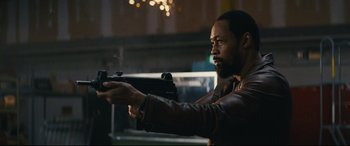 Movie still from “Nobody” (2021), directed by Ilya Naishuller – A man in a brown jacket is holding a gun; Medium shot, Low angle