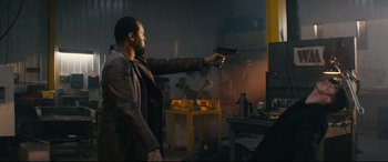 Movie still from “Nobody” (2021), directed by Ilya Naishuller – A man holding a gun in a room with a table; Medium shot, Over the shoulder angle